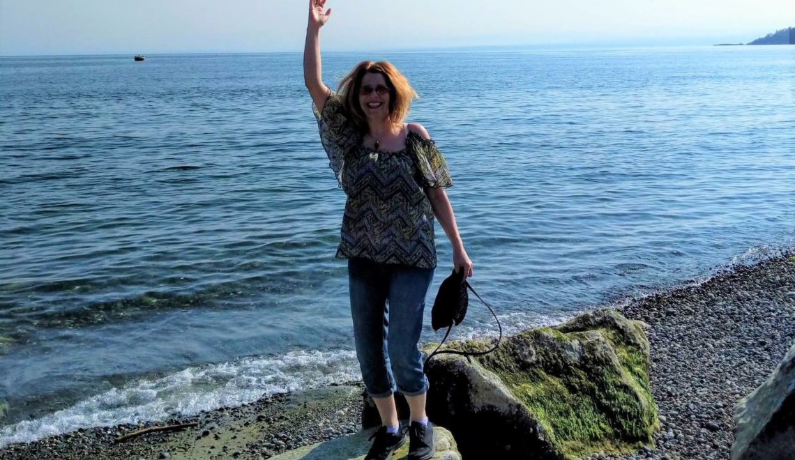 A photo of a woman standing on top of a rock by the ocean.