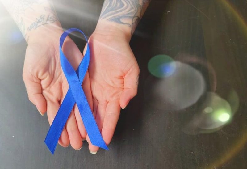 A photo of a person's hand holding a blue ribbon to symbolize Arthritis Awareness Month.