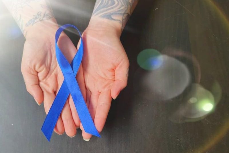 Une photo de la main d'une personne tenant un ruban bleu pour symboliser le Mois de la sensibilisation à l'arthrite.